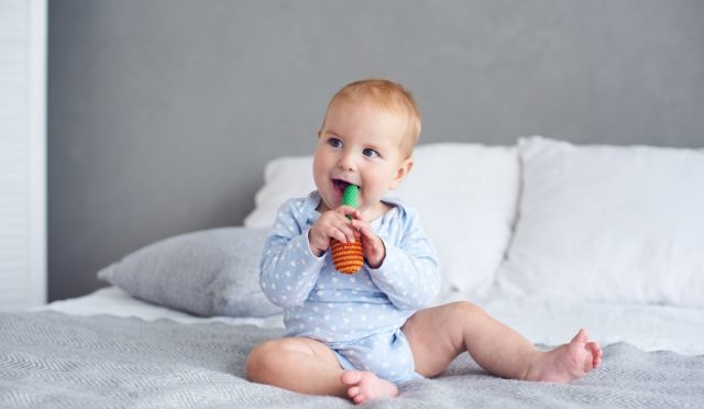 Cute 8 months baby boy playing with knitted toy on bed at home